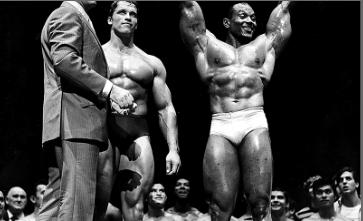 Joe Weider onstage beside two bodybuilders posing